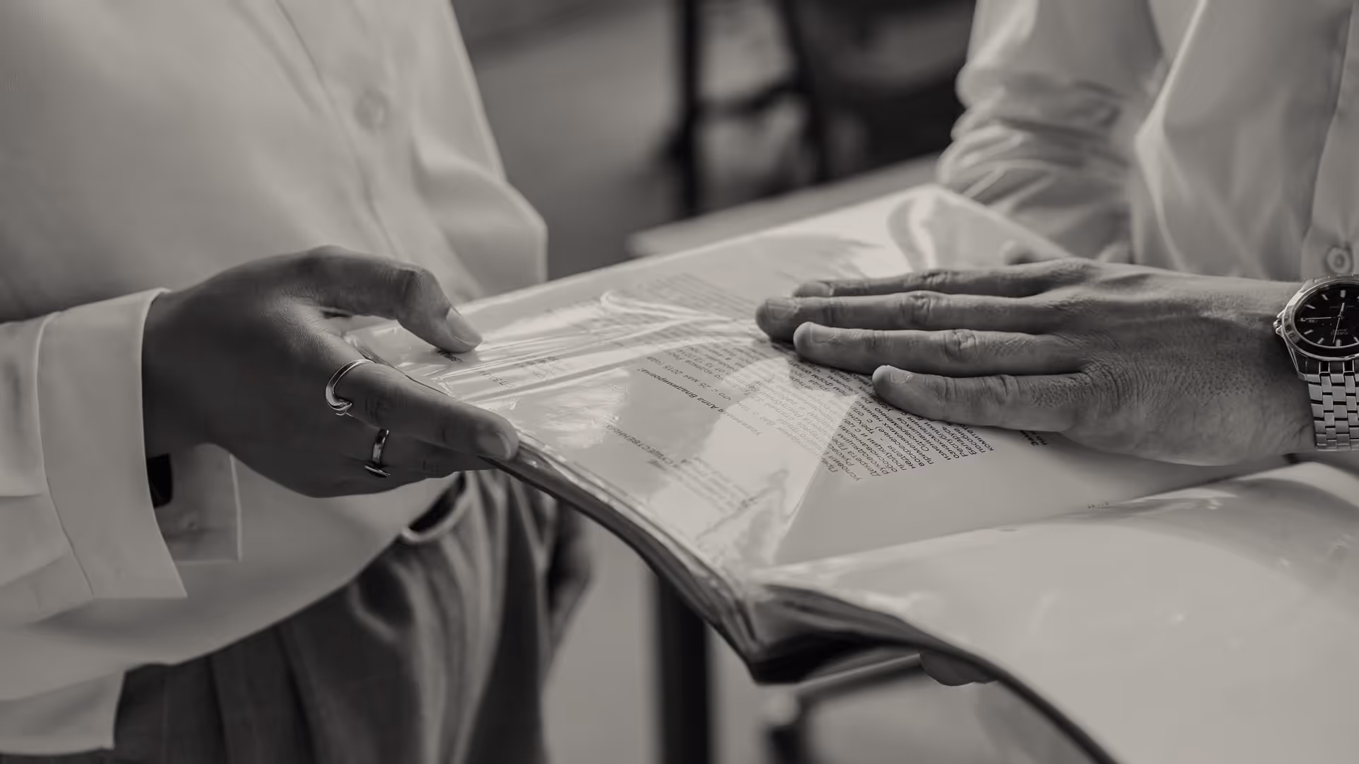 Two people wearing white shirts exchanging and reviewing a plastic-covered document.