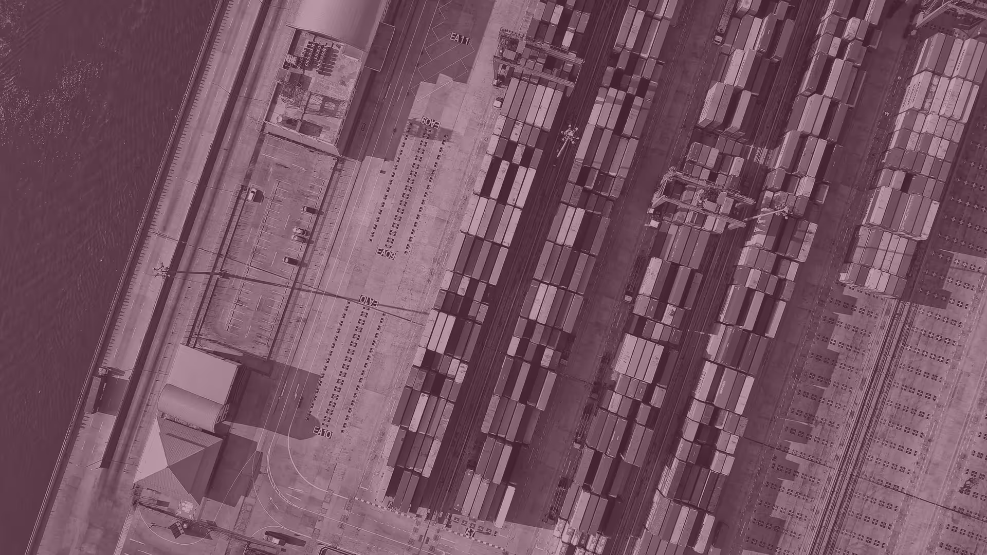 Aerial view of a busy shipping port with rows of stacked cargo containers and cranes along the waterfront.