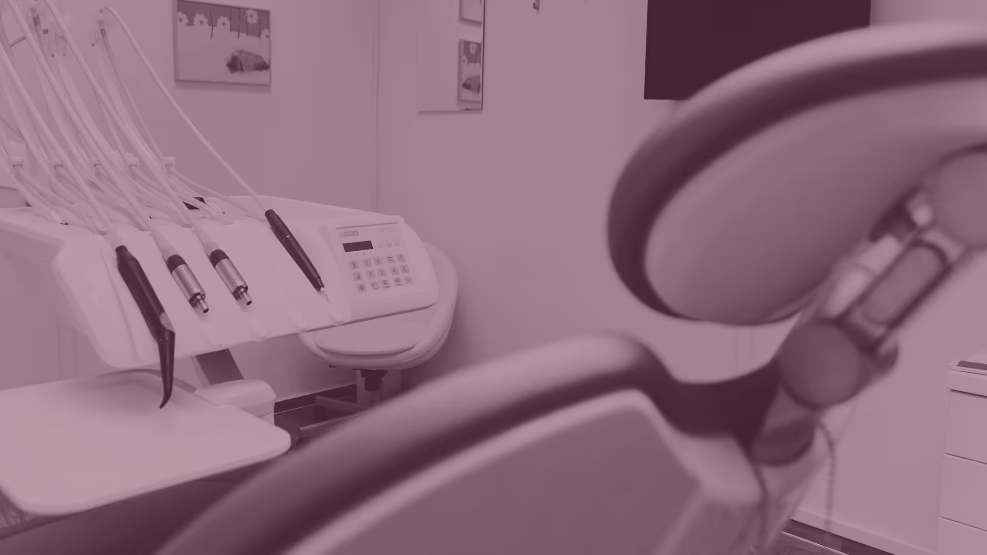 Close-up of dental equipment including handpieces and control panel next to a dental chair in a clinic room.