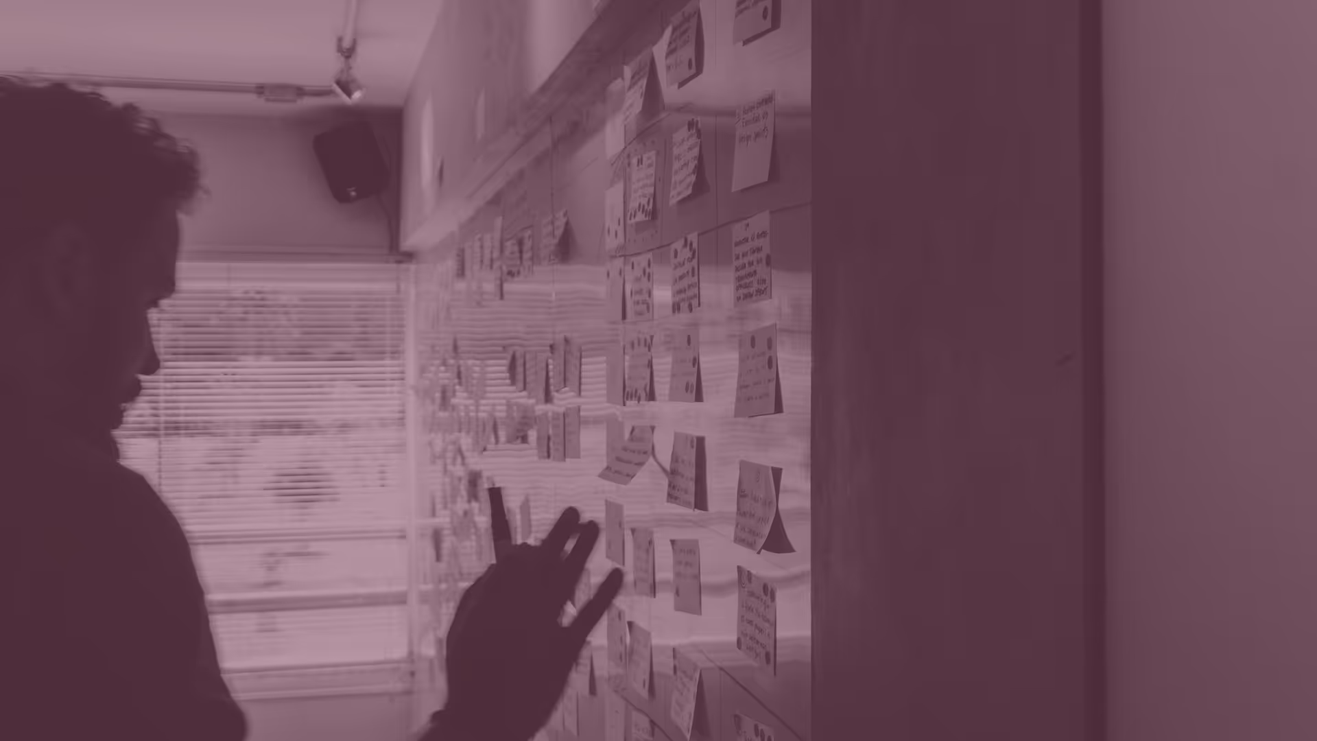 Person reviewing and arranging sticky notes on a wall with a window in the background.