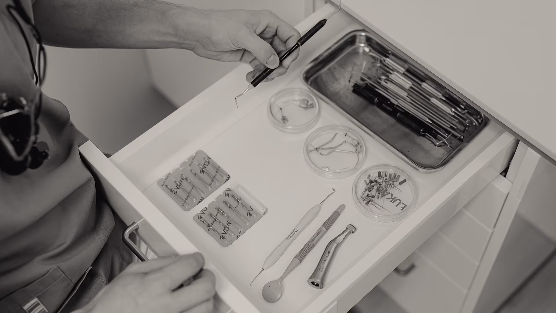 Drawer opened showing dental tools and accessories, including probe, mirror, tweezers, and containers with small dental parts.