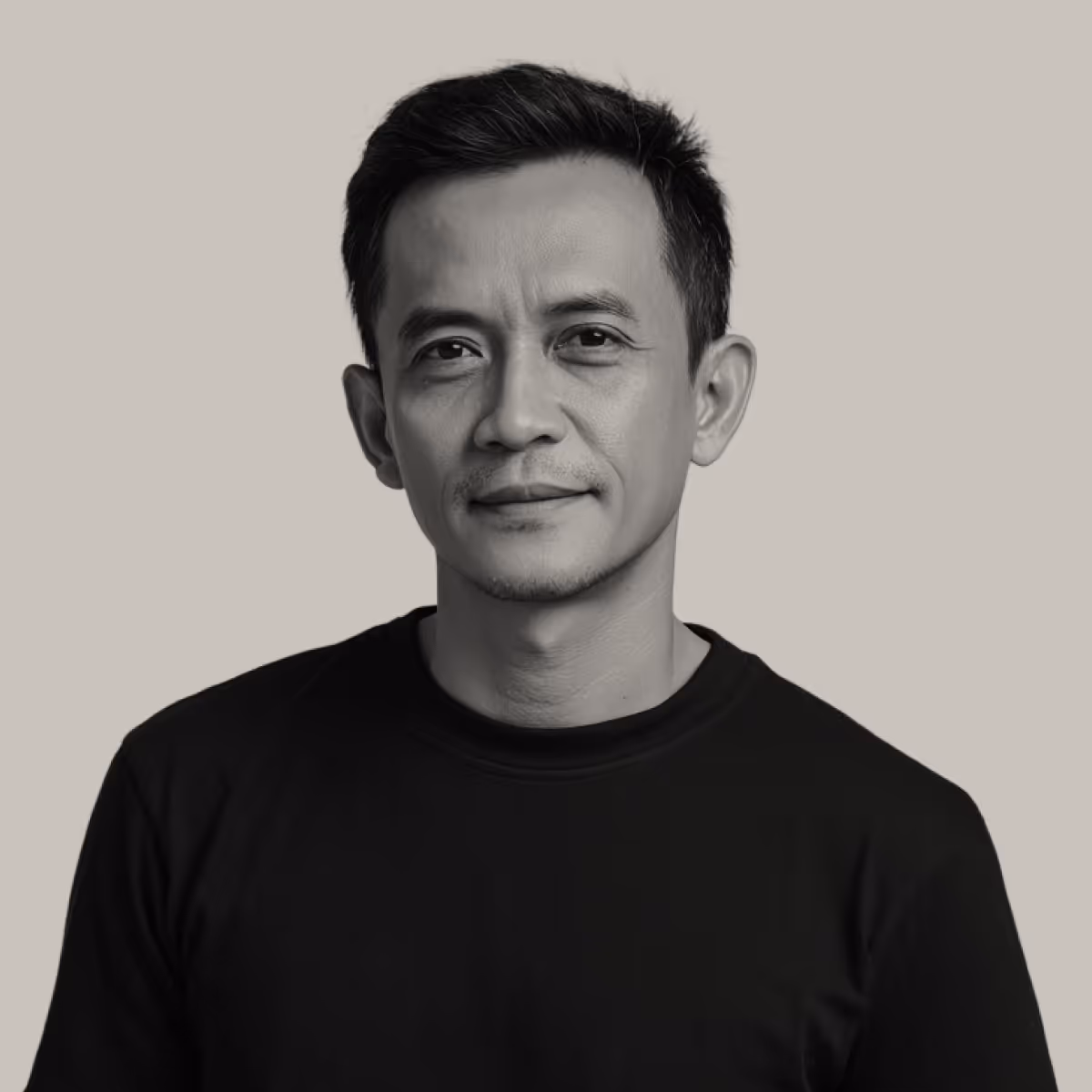 Portrait of a middle-aged man with short black hair wearing a black shirt against a plain light gray background.