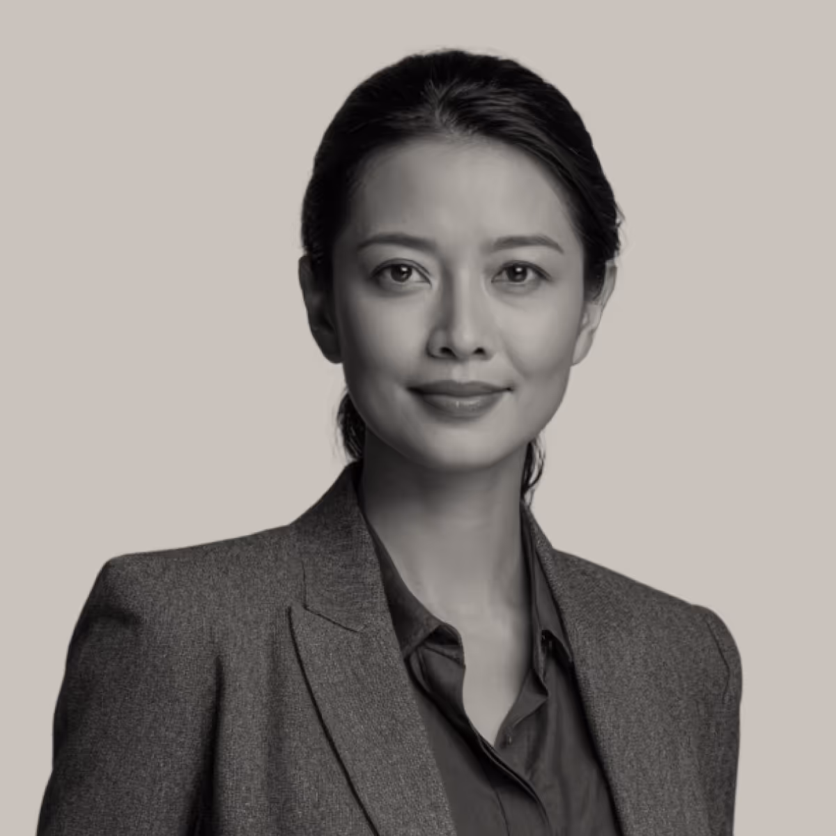 Confident woman with dark hair in a gray blazer and dark shirt against a plain background.